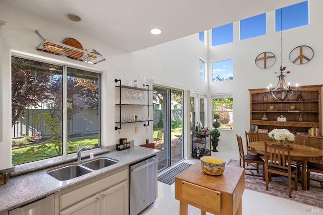 kitchen featuring an inviting chandelier, a towering ceiling, white cabinets, a sink, and dishwasher