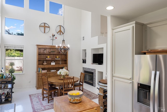 dining room featuring baseboards, a notable chandelier, a glass covered fireplace, a high ceiling, and recessed lighting