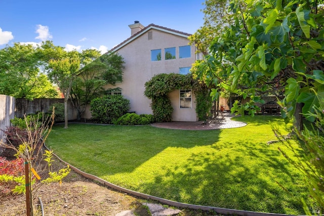 back of property with fence, stucco siding, a chimney, a patio area, and a lawn