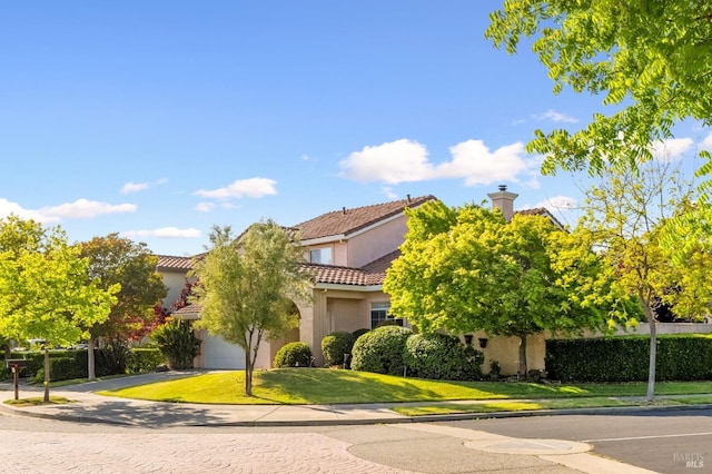 view of front of home featuring an attached garage, a tile roof, a front lawn, stucco siding, and a chimney