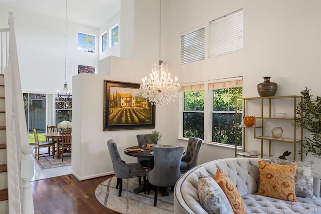 dining room featuring a notable chandelier, a wealth of natural light, wood finished floors, and a towering ceiling