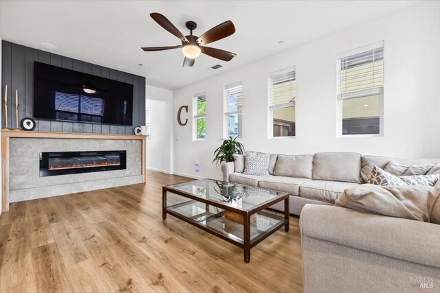 living area with a glass covered fireplace, a ceiling fan, baseboards, wood finished floors, and visible vents