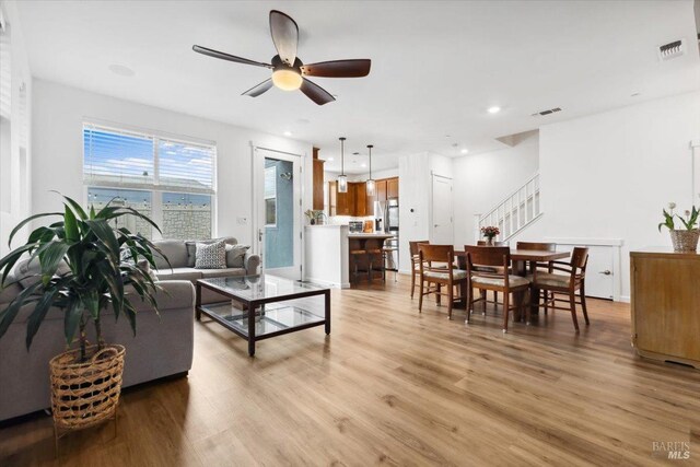 living area featuring light wood-style flooring, a ceiling fan, recessed lighting, visible vents, and stairway