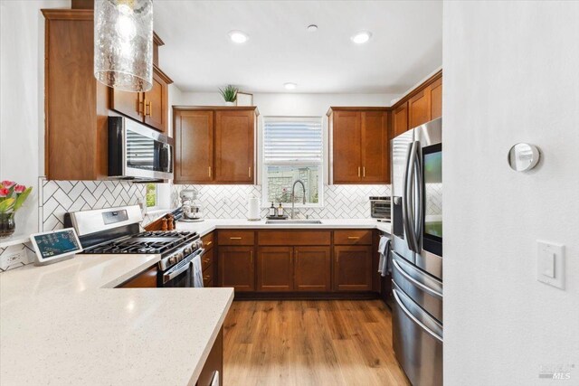 kitchen with brown cabinets, appliances with stainless steel finishes, a sink, light wood-style flooring, and tasteful backsplash