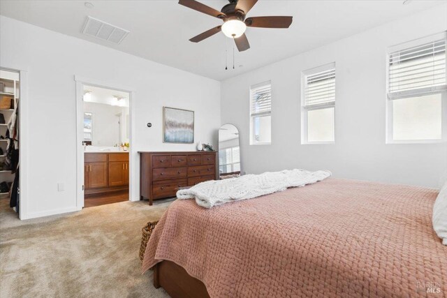 bedroom featuring a walk in closet, light colored carpet, visible vents, a closet, and ensuite bath