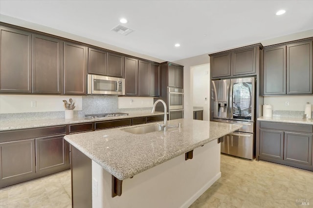 kitchen featuring dark brown cabinetry, appliances with stainless steel finishes, light stone countertops, a sink, and visible vents