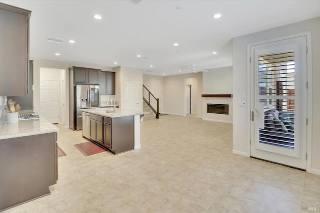 kitchen featuring light stone counters, a sink, stainless steel fridge with ice dispenser, recessed lighting, and visible vents