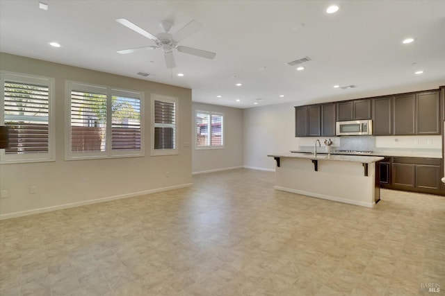 kitchen with visible vents, baseboards, open floor plan, a kitchen breakfast bar, and stainless steel microwave