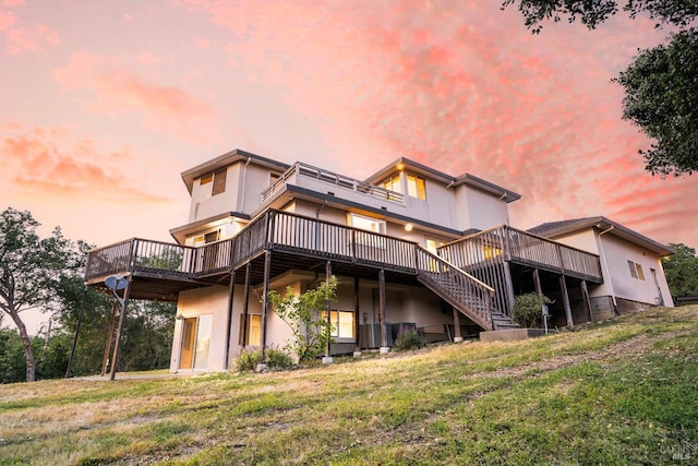 rear view of house featuring a wooden deck, stucco siding, and a yard