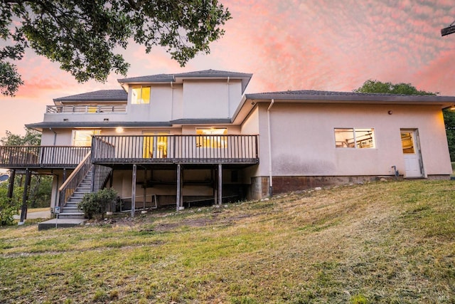 back of house at dusk with a lawn, a wooden deck, stucco siding, and stairway
