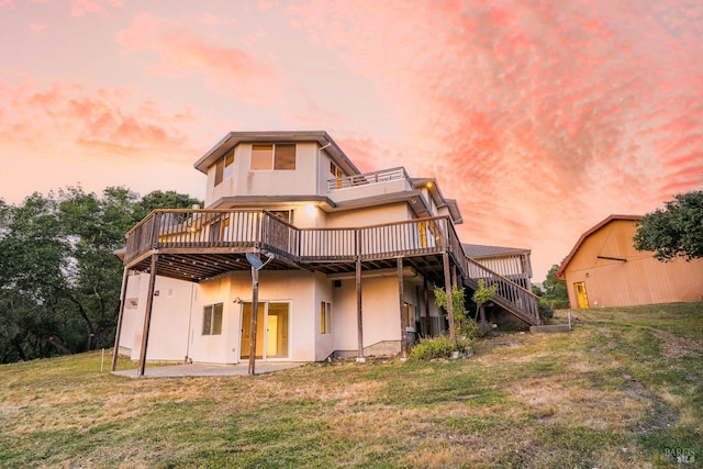 back of property at dusk featuring stairs, a wooden deck, stucco siding, a patio area, and a lawn