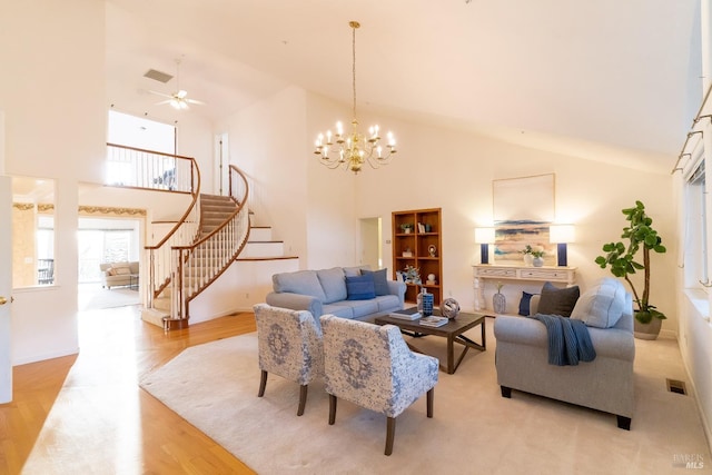 living area with visible vents, light wood-type flooring, high vaulted ceiling, ceiling fan with notable chandelier, and stairs