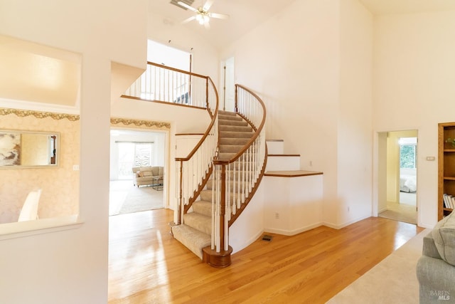 staircase with a healthy amount of sunlight, high vaulted ceiling, baseboards, and wood finished floors