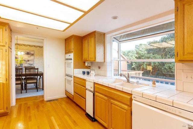 kitchen featuring visible vents, decorative backsplash, white appliances, light wood-style floors, and a sink