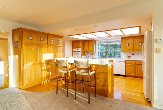 kitchen featuring white appliances, a breakfast bar area, a center island, tile countertops, and backsplash