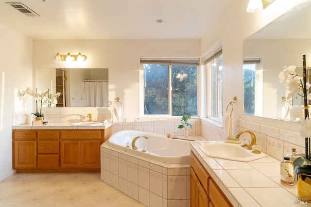 bathroom featuring visible vents, two vanities, a sink, and a garden tub