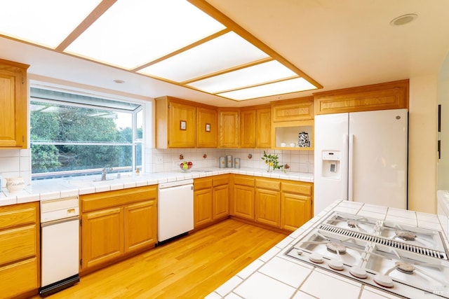kitchen featuring a sink, tasteful backsplash, light wood-type flooring, and white appliances