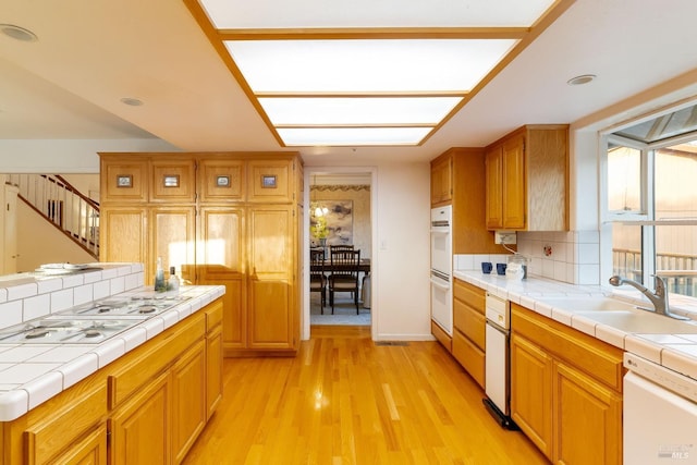 kitchen featuring white appliances, light wood-type flooring, tile countertops, a sink, and backsplash