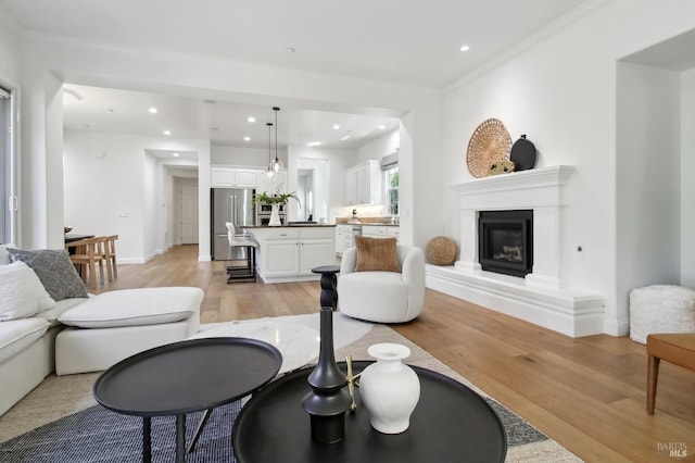 living area featuring crown molding, baseboards, a glass covered fireplace, light wood-style floors, and recessed lighting