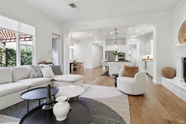 living area featuring light wood finished floors, a fireplace with raised hearth, recessed lighting, visible vents, and ornamental molding