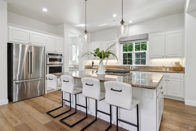 kitchen with stone countertops, a center island, white cabinetry, a sink, and appliances with stainless steel finishes