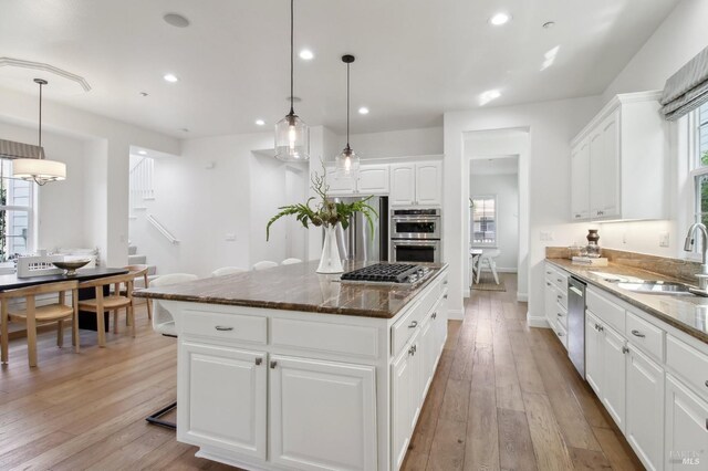kitchen with a sink, stainless steel appliances, dark stone countertops, and a healthy amount of sunlight