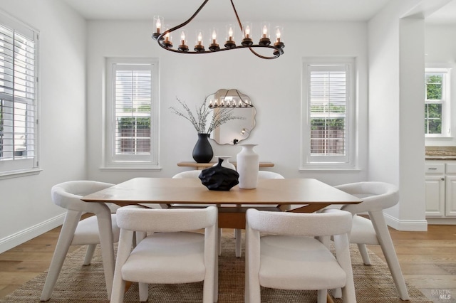 dining space featuring baseboards, a notable chandelier, a healthy amount of sunlight, and light wood-style floors