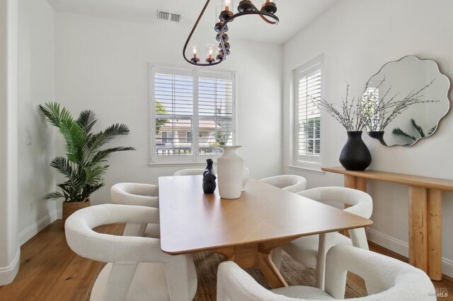 dining area featuring baseboards, an inviting chandelier, wood finished floors, and visible vents