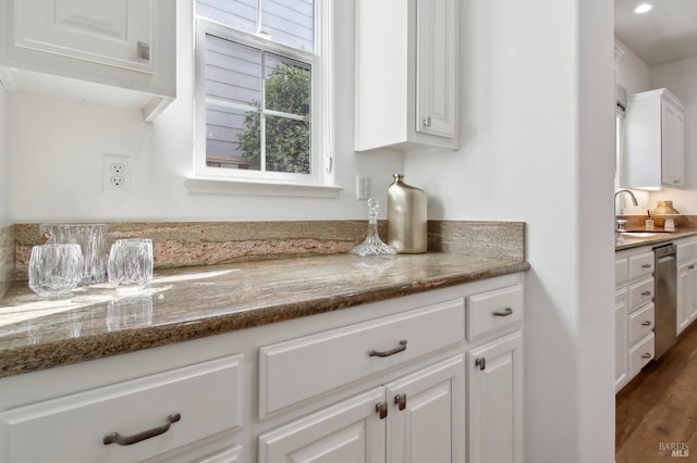 kitchen featuring wood finished floors, stone countertops, white cabinets, a sink, and dishwasher