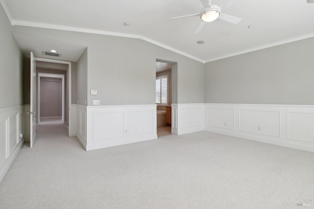 spare room with crown molding, ceiling fan, light colored carpet, wainscoting, and visible vents