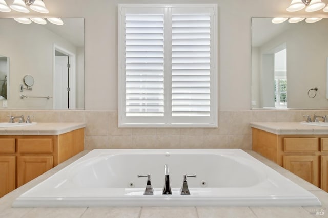 full bathroom with a notable chandelier, two vanities, a sink, and a jetted tub
