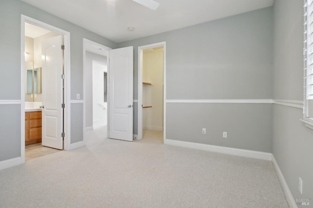 unfurnished bedroom featuring baseboards, ensuite bathroom, light carpet, and a spacious closet