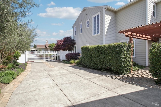 view of home's exterior featuring a gate, fence, a pergola, and concrete driveway