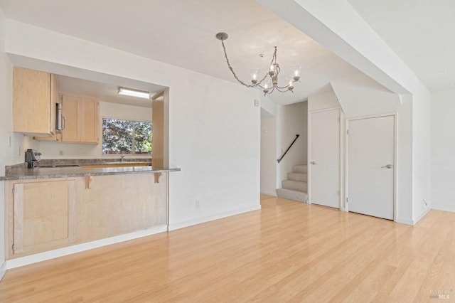 unfurnished dining area featuring light wood-type flooring, stairway, baseboards, a sink, and a notable chandelier