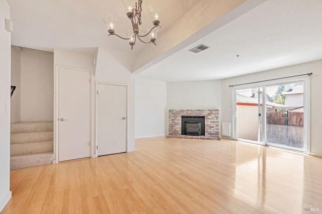 unfurnished living room with an inviting chandelier, a fireplace, light wood finished floors, and visible vents