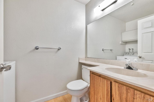 half bathroom featuring vanity, wood finished floors, toilet, baseboards, and separate washer and dryer