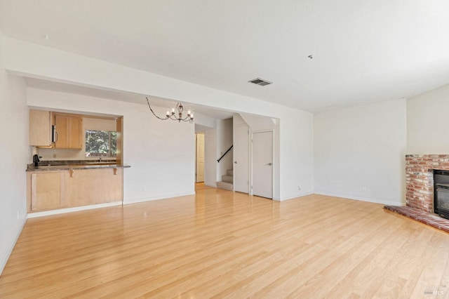 unfurnished living room with visible vents, stairway, baseboards, light wood finished floors, and a notable chandelier