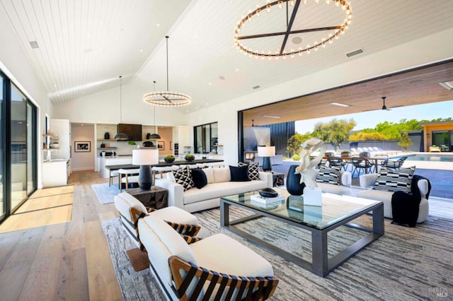 living room with high vaulted ceiling, an inviting chandelier, visible vents, and light wood-type flooring