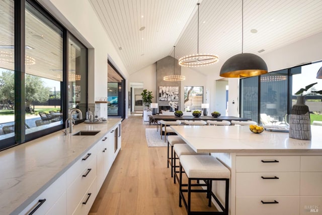 kitchen with modern cabinets, light wood-type flooring, white cabinetry, a sink, and a notable chandelier