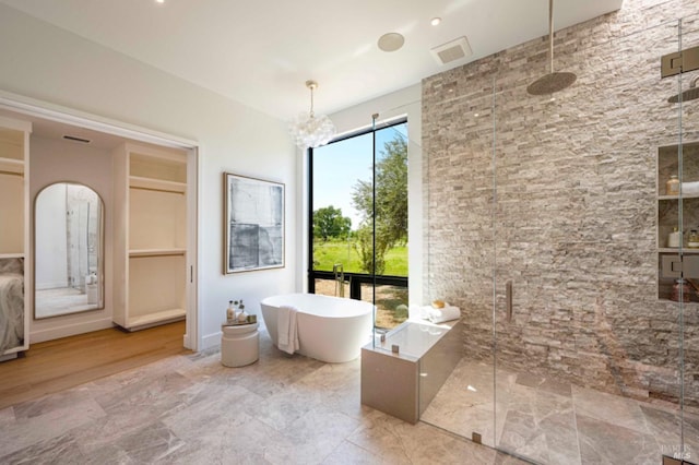 full bath featuring an inviting chandelier, a soaking tub, a stall shower, and visible vents