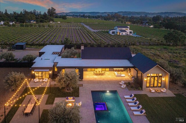 pool at dusk featuring an outdoor pool, a patio area, a mountain view, an outdoor fire pit, and a rural view