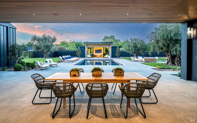 patio terrace at dusk with a fenced backyard, a fenced in pool, an outdoor structure, and outdoor dining area