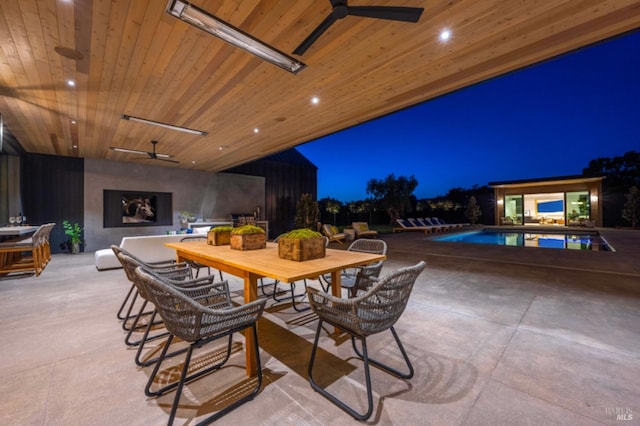 patio at twilight with outdoor dining area, ceiling fan, a fireplace, and an outdoor pool