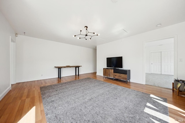 unfurnished living room with baseboards, wood finished floors, and a notable chandelier