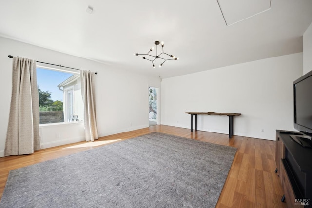 unfurnished living room featuring baseboards, a notable chandelier, and wood finished floors
