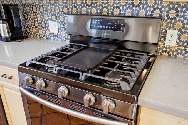 interior details with backsplash, stainless steel gas stove, and wallpapered walls