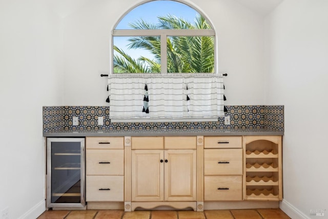 bar featuring wine cooler, baseboards, light tile patterned floors, a dry bar, and backsplash