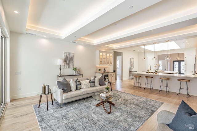living room featuring light wood-style floors, baseboards, a tray ceiling, and visible vents