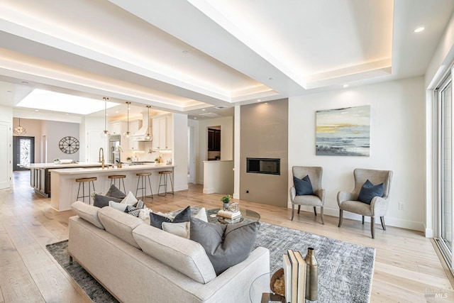 living room with baseboards, light wood-style flooring, a raised ceiling, and recessed lighting