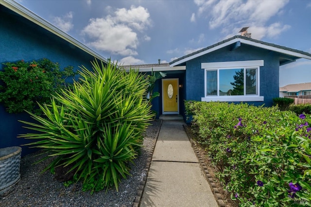 view of exterior entry featuring stucco siding and a chimney